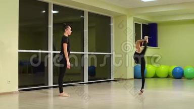 两个身材苗条的女孩姐妹穿着黑色运动服的艺术体操运动员在健身房做热身运动和艺术体操